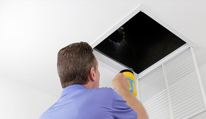 Man inspecting an air duct with a flashlight