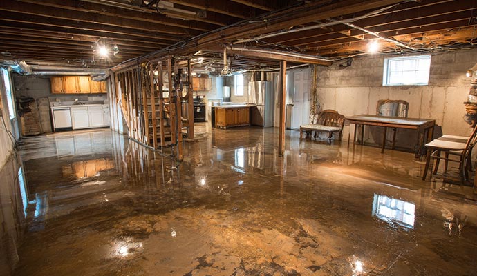An unfinished basement with exposed wooden ceiling joists and concrete walls, showing significant flooding covering the entire floor