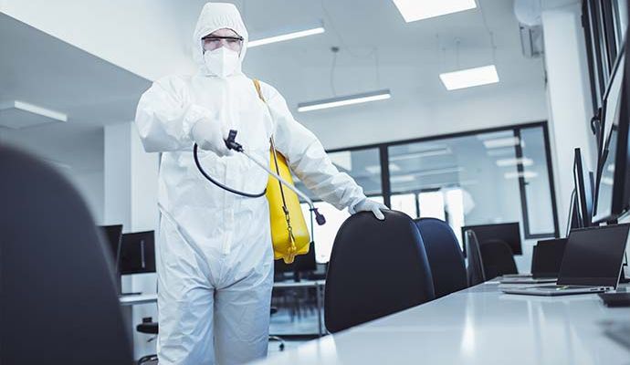 Man in protective suit and face mask spraying for disinfection in the office
