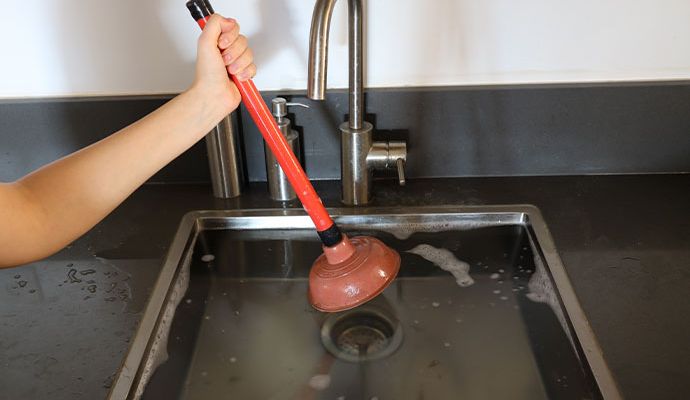 Plumber using a plunger to clear an overflow kitchen sink